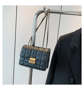 Detail of black quilted shoulder bag with gold chain strap and metallic buckle