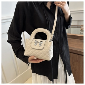 Detail of beige quilted crossbody bag with a silver bow clasp worn by a model