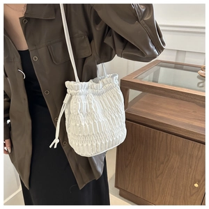 Detail of white drawstring bucket bag with vertical pleated texture and leather shoulder strap