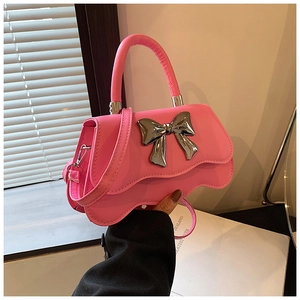 Détail d'un sac à main rose vif avec un nœud argenté métallique et un bord ondulé