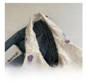 Détail de la bandoulière de sac tricoté blanc avec franges et broderies de fleurs