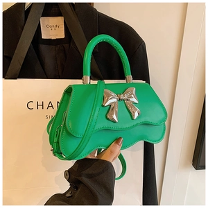 Détail d'un sac à main vert vif avec un grand nœud métallique et un design ondulé