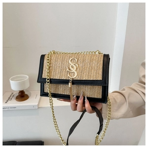 Close-up of woven straw beach bag featuring black trim and gold SS logo with chain strap