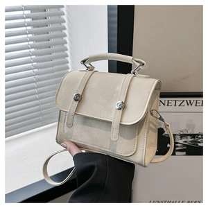 Detail of minimalist cream leather handbag featuring silver round buckle and top handle