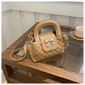 Close-up of quilted beige handbag featuring silver bow hardware and top handle detail