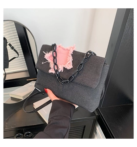 Detail of denim shoulder bag featuring a pink frayed star patch and black chain strap