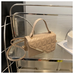 Dettaglio borsa a tracolla trapuntata beige con motivi geometrici e barra dorata