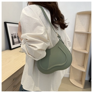 Detail of a light green minimalist underarm bag featuring curved seams and slim shoulder strap
