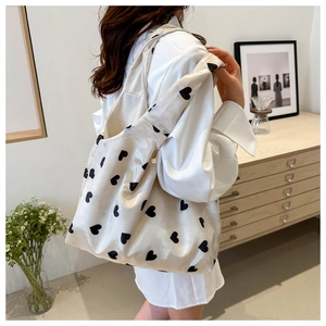 Vue d'épaule d'un sac cabas en tricot crème avec motifs de cœurs noirs en intérieur