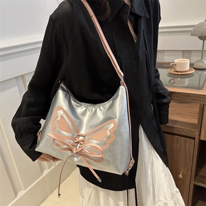 Chic silver metallic shoulder bag with pink butterfly bow detail worn by a model