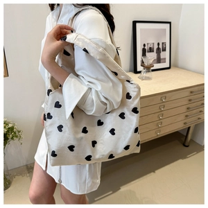 Détail d'un sac cabas en tricot beige avec des cœurs noirs porté sur l'épaule