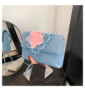 Detail of blue denim shoulder bag with pink frayed star patch and plastic chain strap