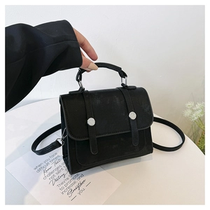 Detail of black textured crossbody bag with silver rivet buckles and slim shoulder strap