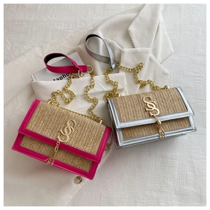Close-up of woven straw handbag featuring gold chain strap and metal S logo with tassel