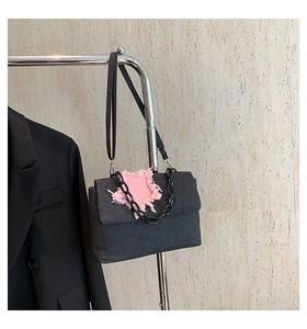 Detail of a black denim bag with a pink fringed heart patch and matte black chain