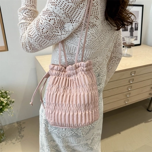 Light pink drawstring bucket bag with vertical pleated texture shown on a female model