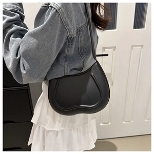 Close-up of heart-shaped black matte leather shoulder bag with decorative line patterns