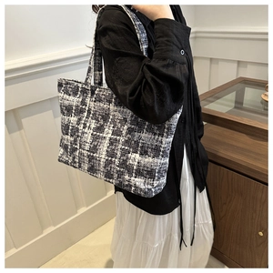 Close-up of black and white tweed tote bag with textured fabric and long shoulder straps