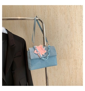 Detail of denim shoulder bag with pink frayed star patch and blue chunky chain strap