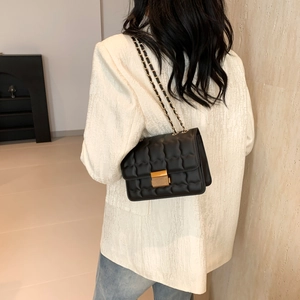 Quilted black crossbody bag with gold hardware and chain strap on a white blazer