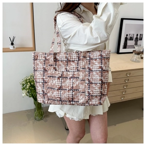 Detail view of a large checkered tweed tote bag with a front pocket in a minimalist setting
