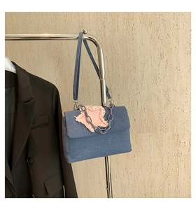 Detail of blue denim crossbody bag featuring a pink frayed star patch and decorative chain