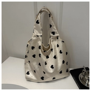 Détail du sac cabas en satin crème avec motifs de cœurs noirs dans un décor minimaliste