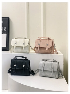 Multiple colors of vintage messenger square bags displayed on a white tiered stand