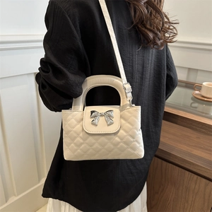 Quilted white shoulder bag with silver bow hardware worn by a model in a stylish room