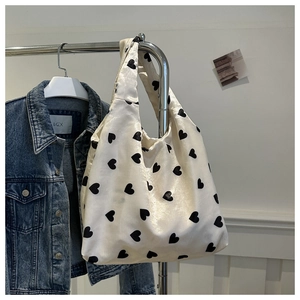 Chic sac fourre-tout tricoté crème avec motifs de cœurs noirs suspendu près d'une veste en jean
