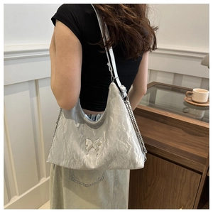 Détail du sac bandoulière argenté plissé avec logo papillon 3D et bandoulière chaîne