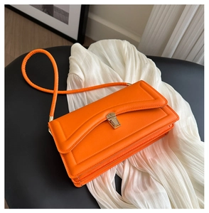 Detail of bright orange faux leather handbag with gold clasp and cylindrical strap