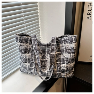 Close-up of black and white tweed tote bag with woven texture and matching shoulder strap