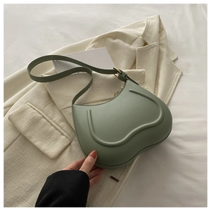 Detail of a green leather heart-shaped shoulder bag with gold metal buckle on a white blazer