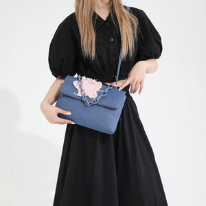 Denim crossbody bag with pink star patch and chunky blue chain worn by a model