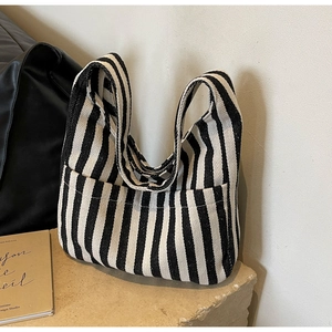 Detail of striped canvas tote bag showing soft texture and side pocket design on stone