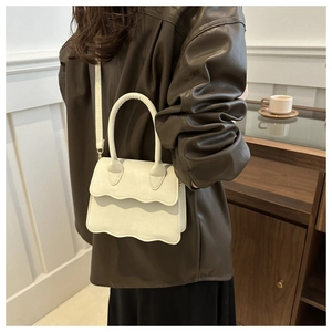 Detail showing white scalloped-edge flap handbag with top handle and leather shoulder strap