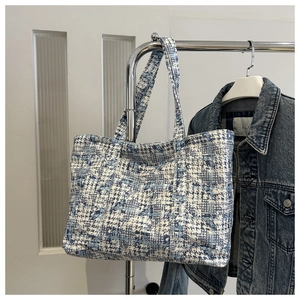 Detail of blue and white tweed woven tote bag with matching shoulder strap on a hanger