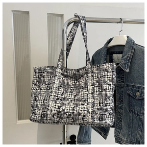 Detail of black and white houndstooth tweed tote bag hanging on a minimalist metal hanger