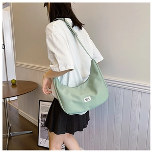 Detail view of a light green nylon crescent crossbody bag worn by a model in casual setting