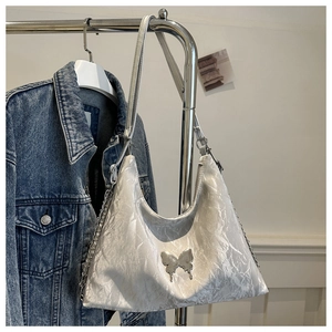 Détail d'un sac à bandoulière blanc texturé avec papillon métallique et chaîne argent