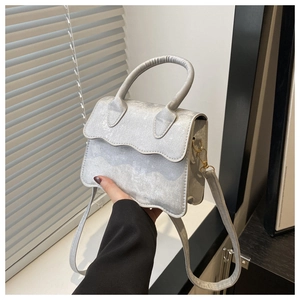 Detail of silver glitter crossbody bag with unique wavy flap and golden hardware