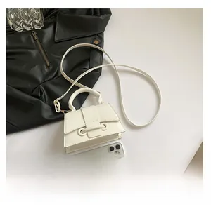 Size comparison of the white mini crossbody bag next to a smartphone and leather jacket