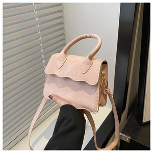 Detail of pink faux suede crossbody bag with elegant wavy scalloped flap edge and gold hardware