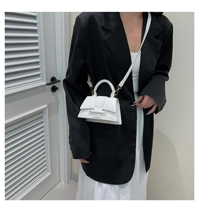 Close-up of a white leather mini bag with circular buckle decoration on a black blazer