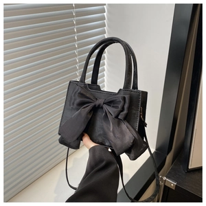 Détail d'un mini sac à main noir avec un grand nœud en satin et une bandoulière mince