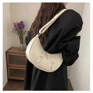 Close-up of cream crescent shoulder bag with silver buckles worn by a model in a blazer