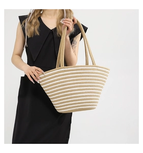 Détail d'un grand sac cabas tissé à rayures kaki et blanc porté à l'épaule par un mannequin