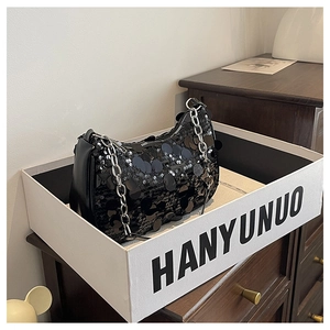 Detail of black sequined crescent bag with silver chain strap in a white branded gift box