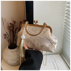 Detail of luxury silk shell bag featuring vintage floral embroidery and green tassel charm